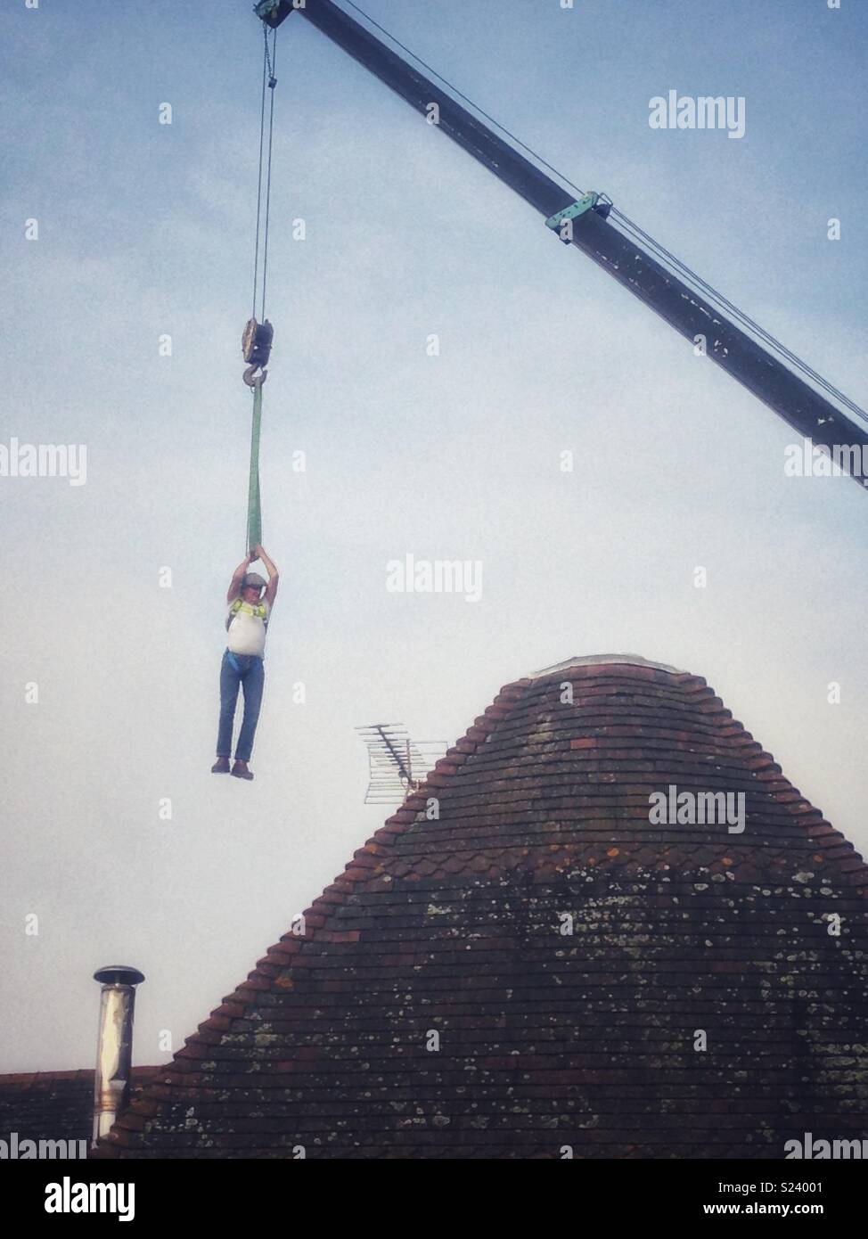 Roofer being lifted above house on crane Stock Photo