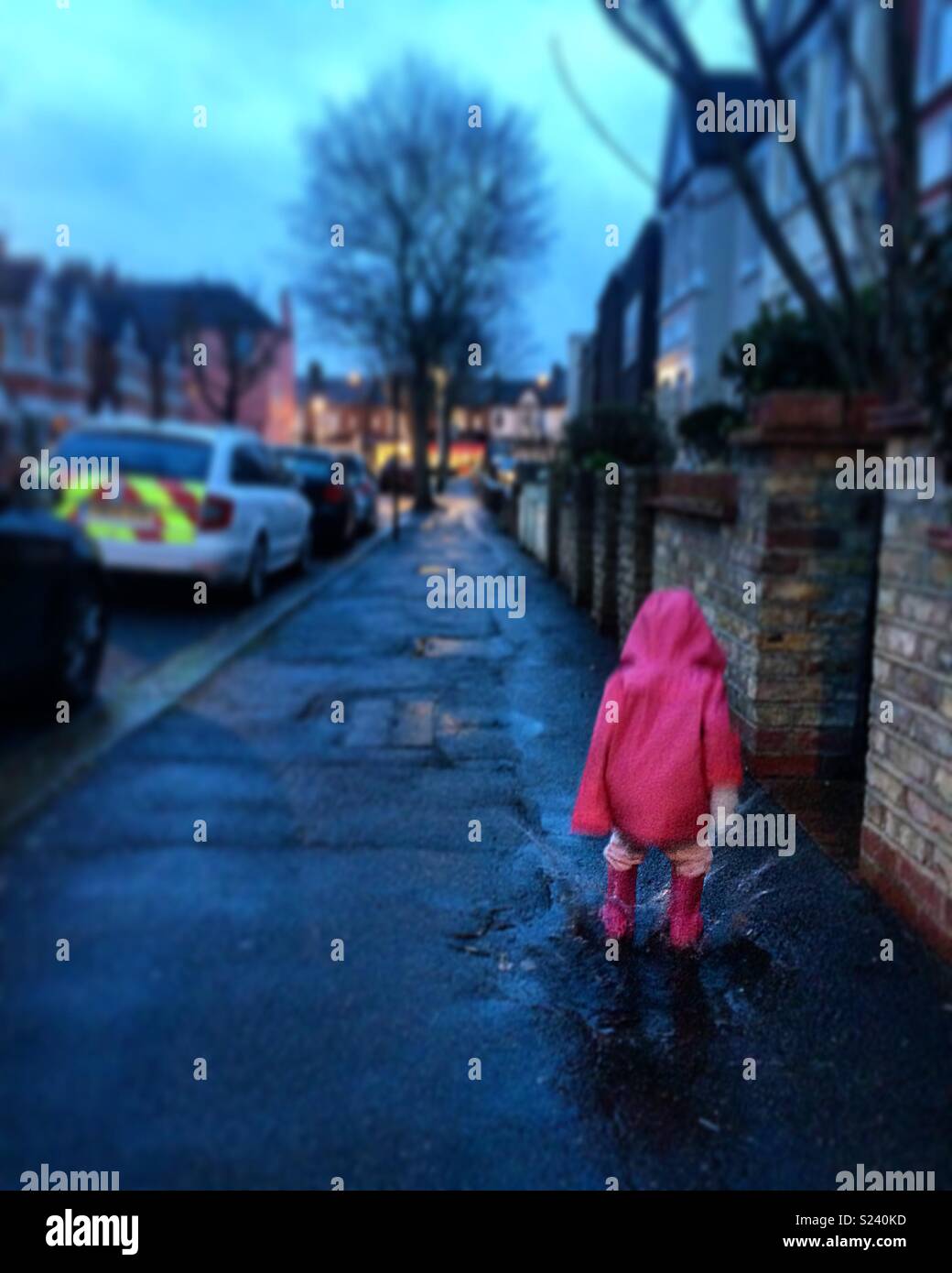 Action shot: little girl dressed in pink jumps in puddle Stock Photo