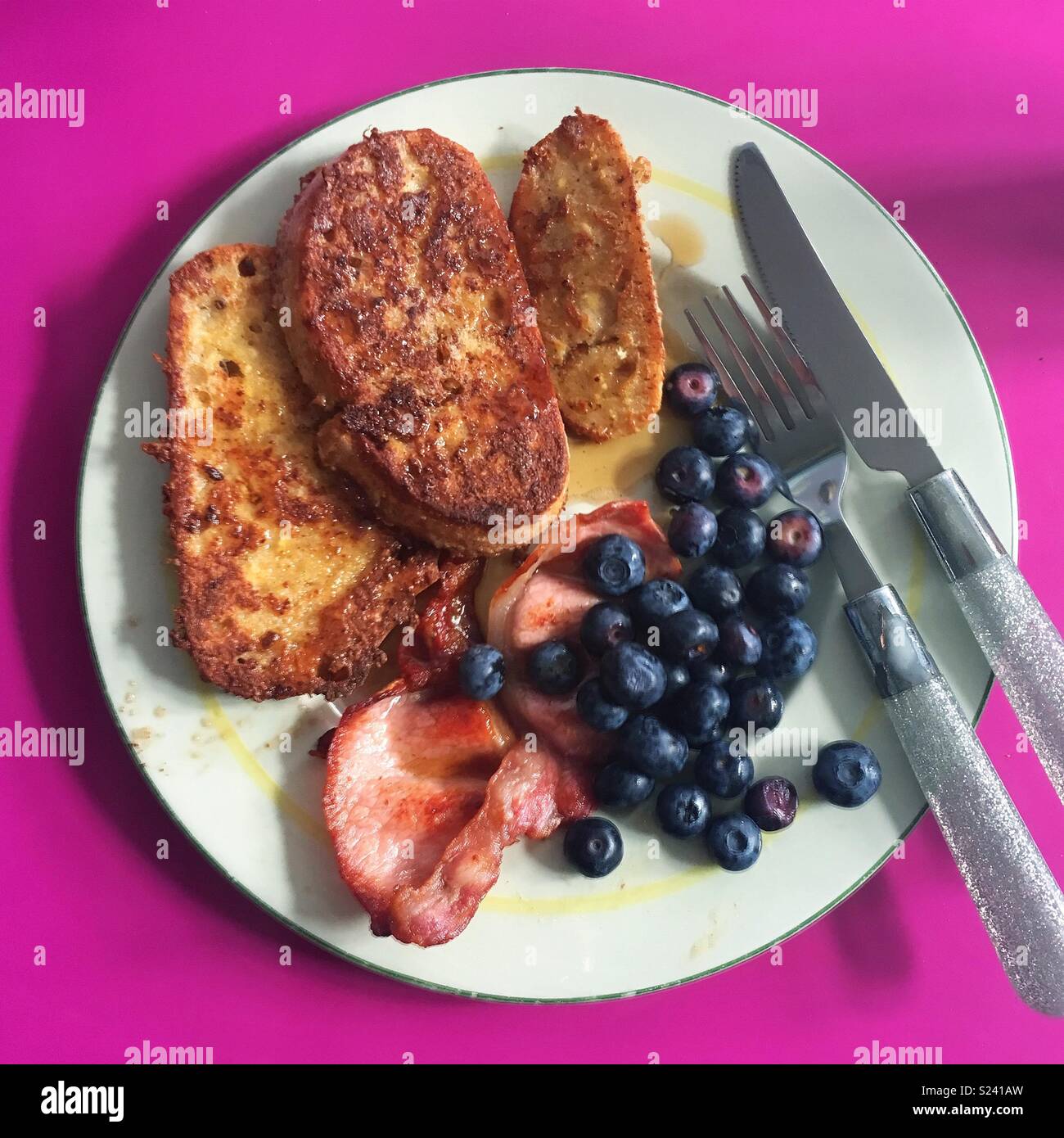 Homemade brunch of French toast, bacon, blueberries and maple syrup. Served on a vintage plate with glittery cutlery on a shocking pink kitchen worktop! Stock Photo