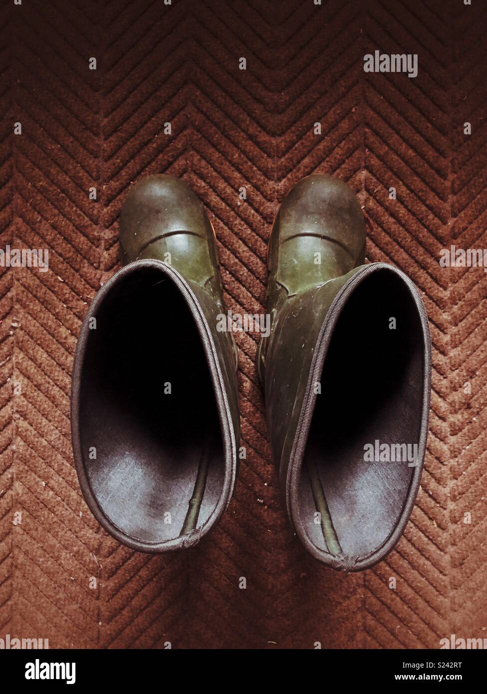 Looking down into empty green Wellington rain boots on a brown floor mat Stock Photo