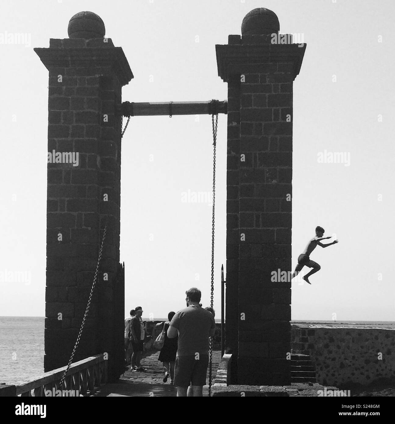 Boy jumping off a bridge into the sea in black and white Stock Photo