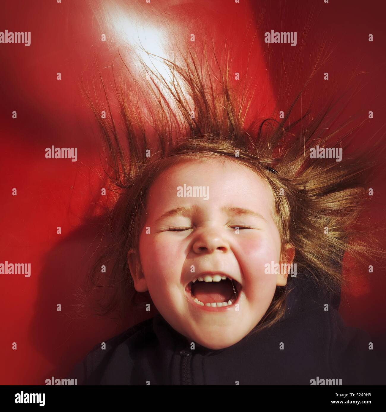 Toddler girl laughing with joy as she slides down a red slide Stock Photo