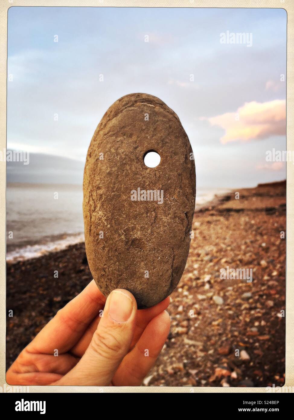 Stone on beach with hole through it. - Smartphone Captured Stock Image