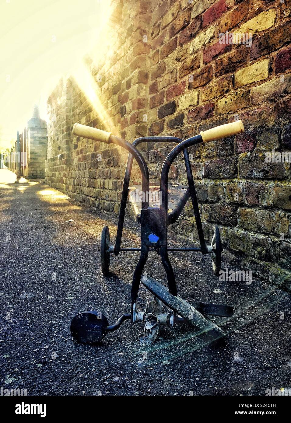 Sad and lonely broken tricycle abandoned on the pavement illuminated by dramatic sunlight, capturing a sense of decay and abandonment - Smartphone Captured Stock Image