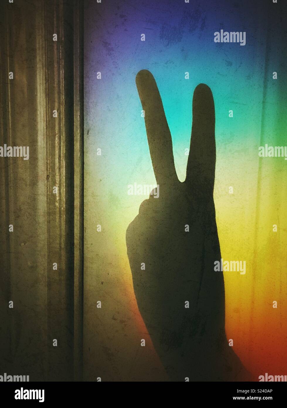 Shadow silhouette of persons hand giving peace symbol against rainbow light Stock Photo