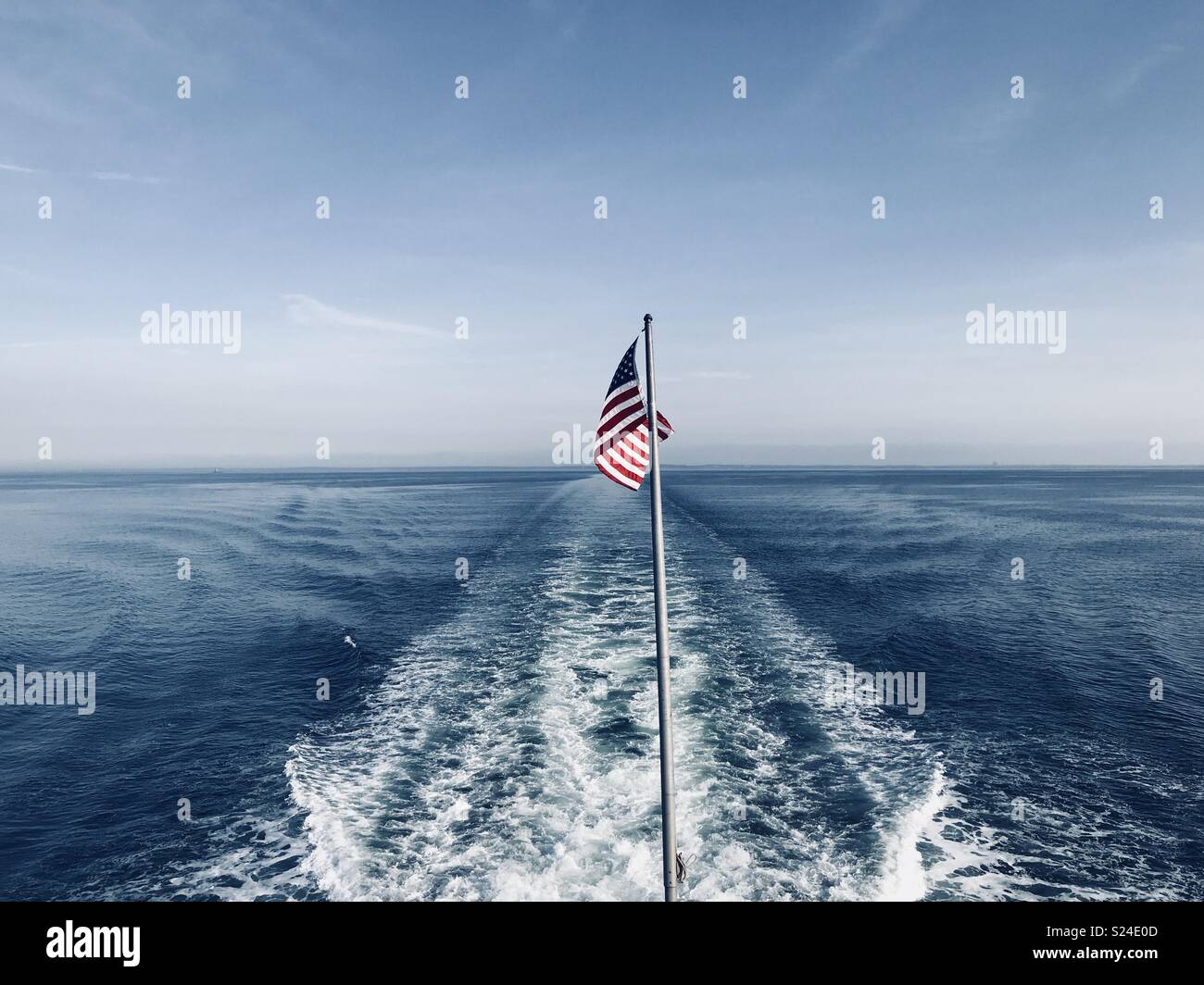 Ferry boat wake with American flag on the flagpole disappearing over the horizon Stock Photo