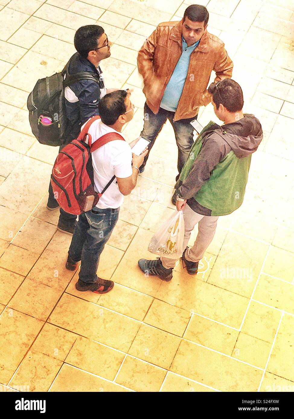 Four men waiting for their train and checking their smartphone - Smartphone Captured Stock Image