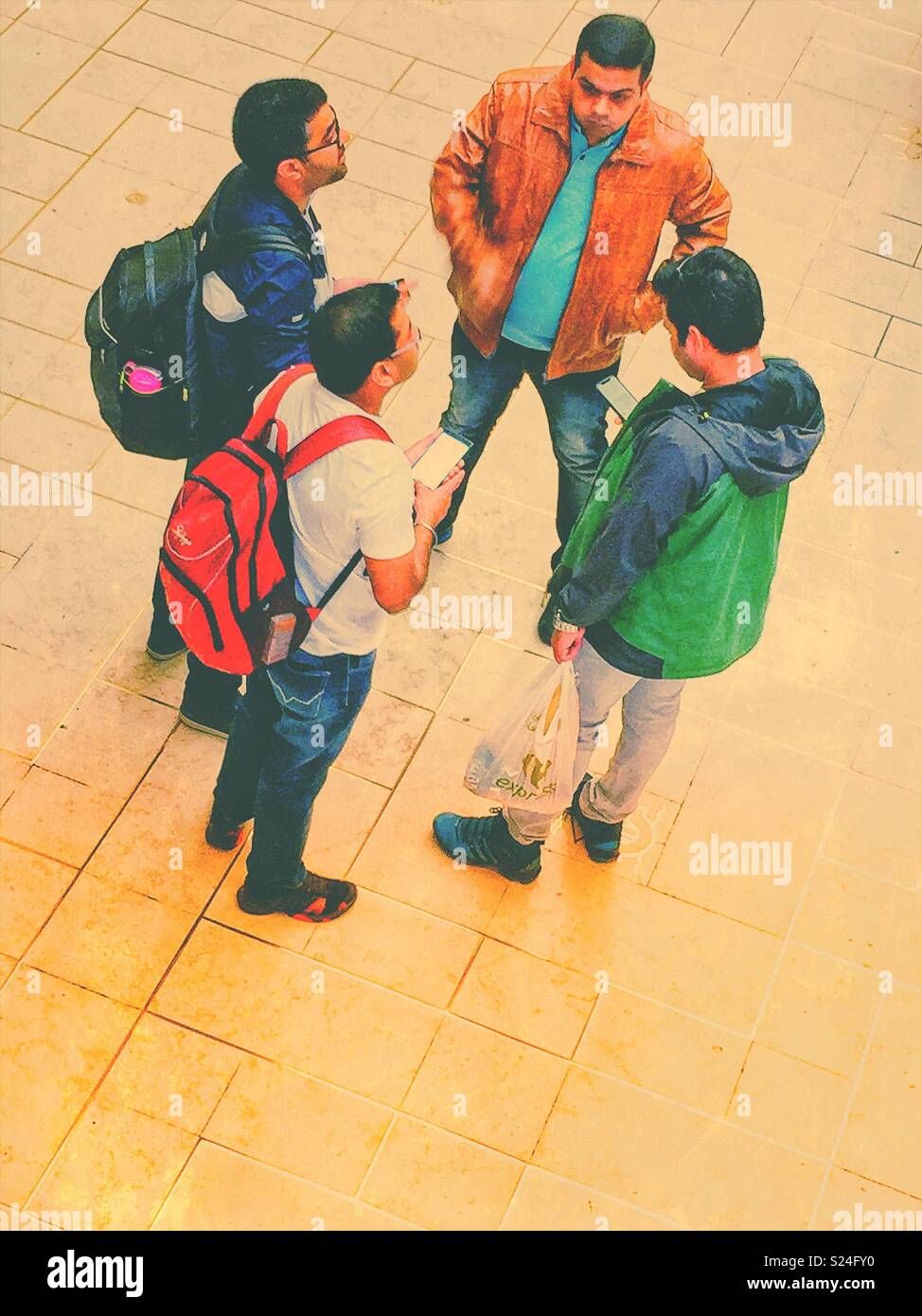 Four men waiting on their train and checking their smartphones - Smartphone Captured Stock Image