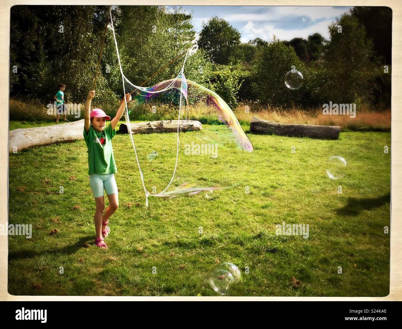 Girl blowing giant bubble in park. - Smartphone Captured Stock Image
