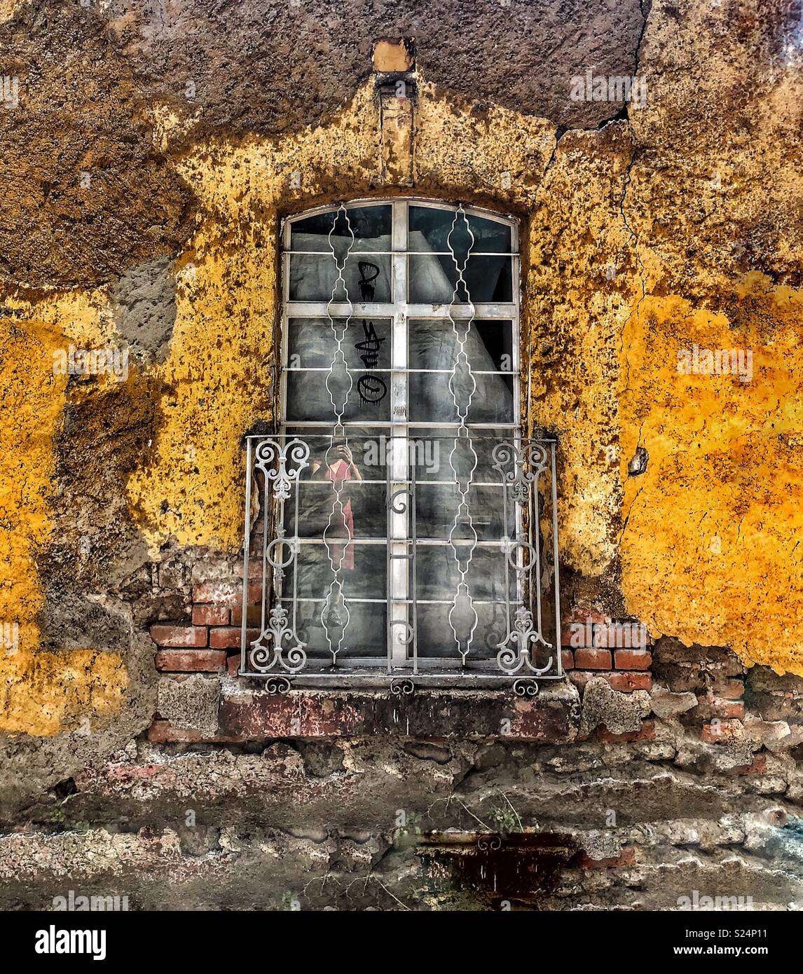 Window with Ironwork on a Yellow Wall with Exposed Brick in Coyoacán, Mexico City Stock Photo