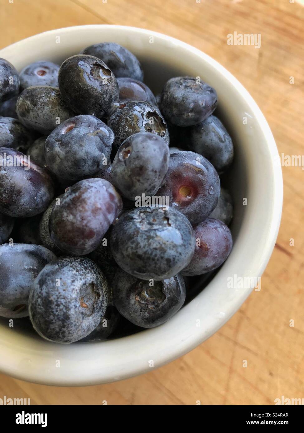 Blueberries in a small white bowl sitting on a wooden table. - Smartphone Captured Stock Image