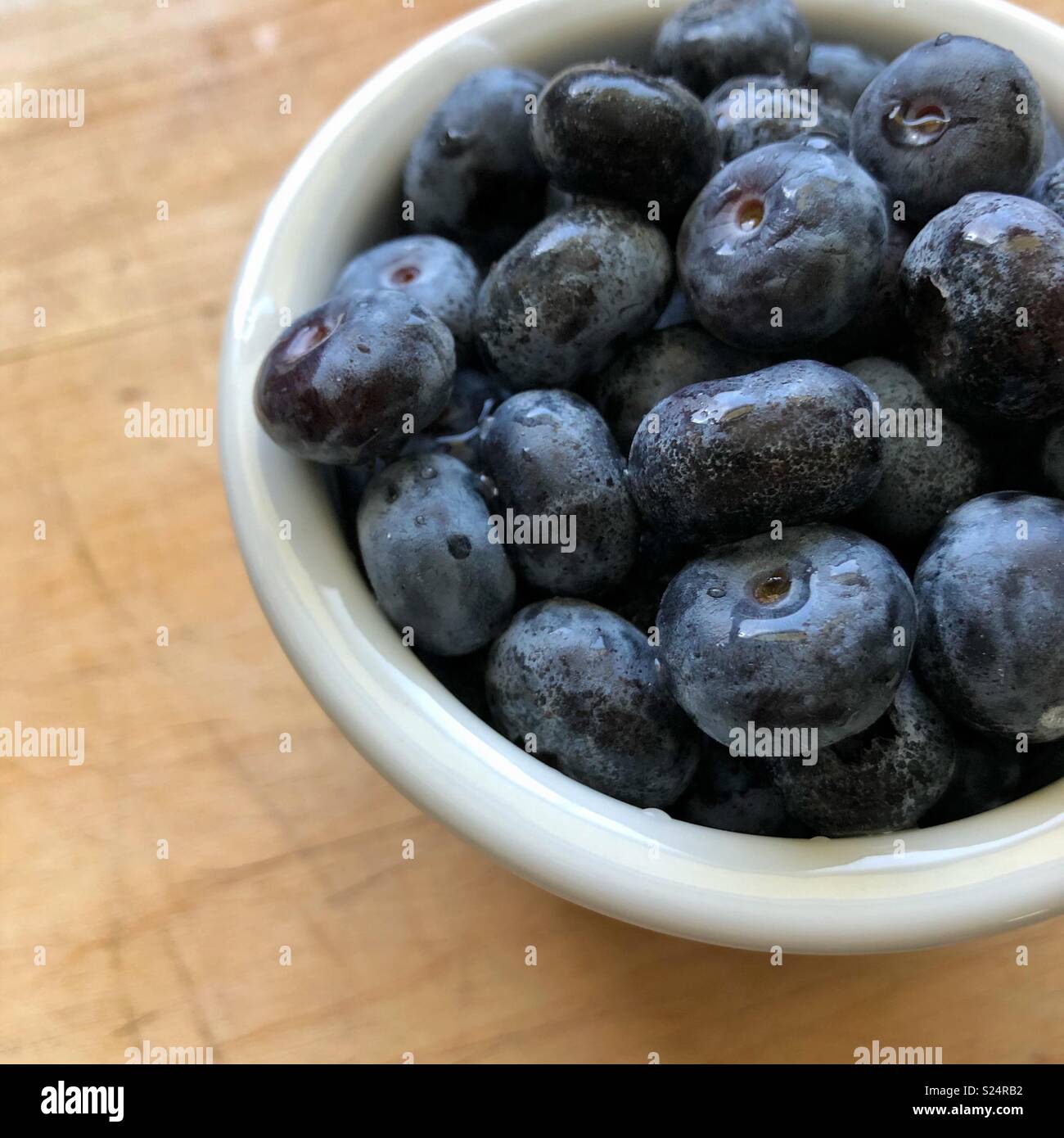 Blueberries in a small white bowl sitting on a wooden table. - Smartphone Captured Stock Image