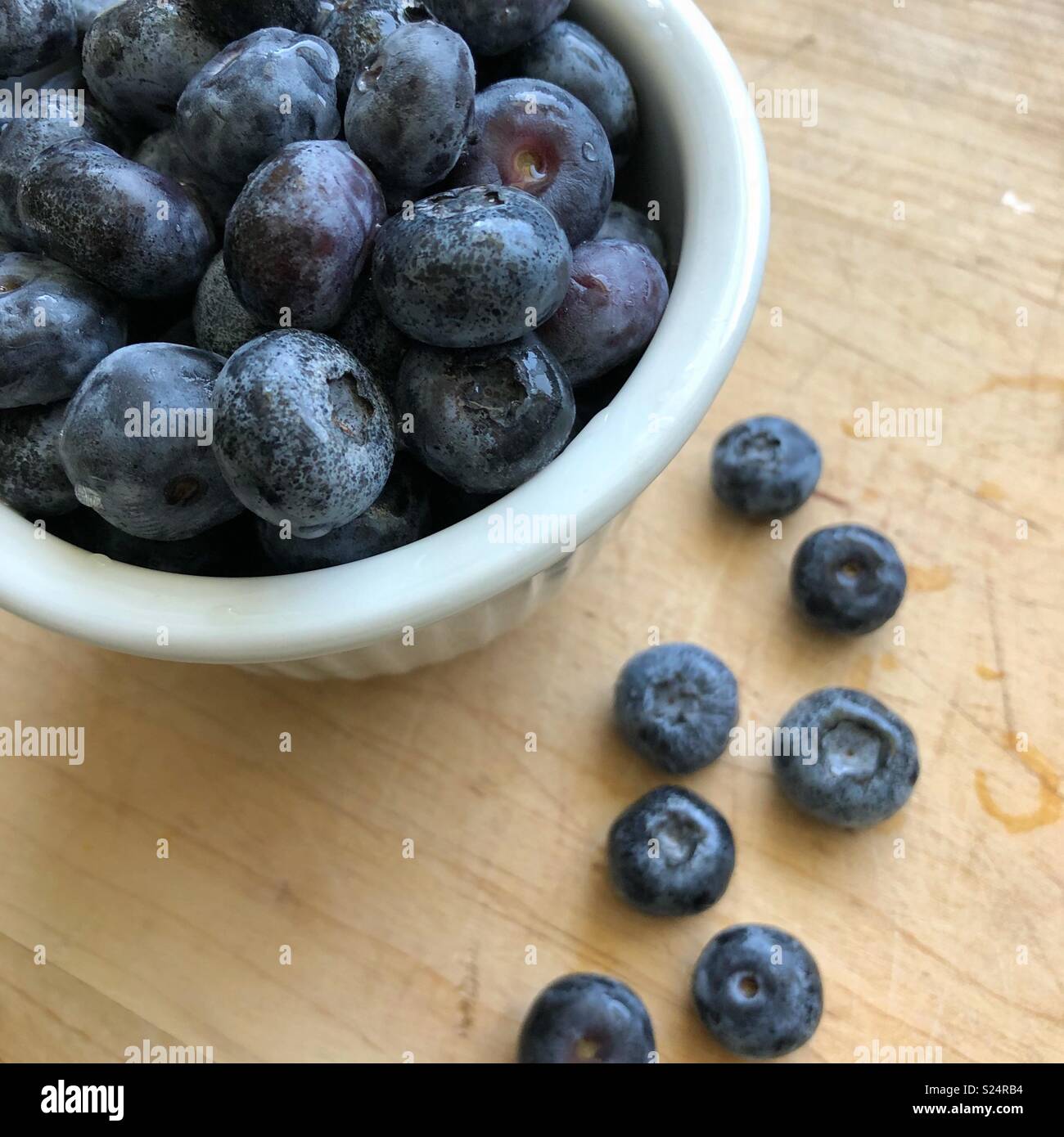 Blueberries in a small white bowl sitting on a wooden table. - Smartphone Captured Stock Image