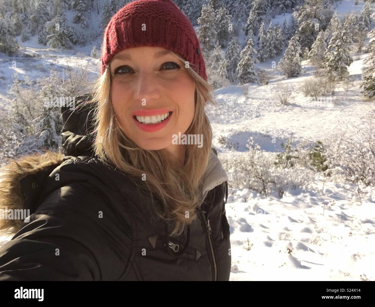 Woman smiling at camera outdoors on a sunny snowy cold winter day. - Smartphone Captured Stock Image