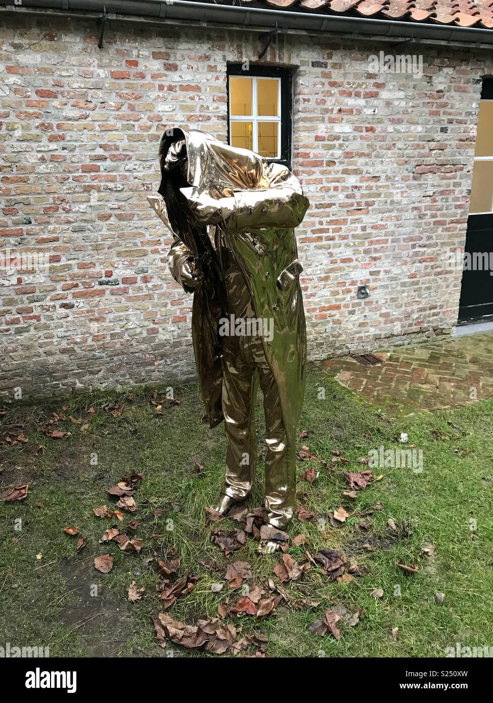 Gold statue of man holding his coat over his head and not wearing any shoes. Bruges, Belgium. Stock Photo