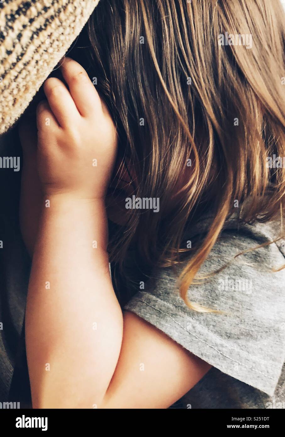 Closeup side view of toddler girl covering face crying Stock Photo