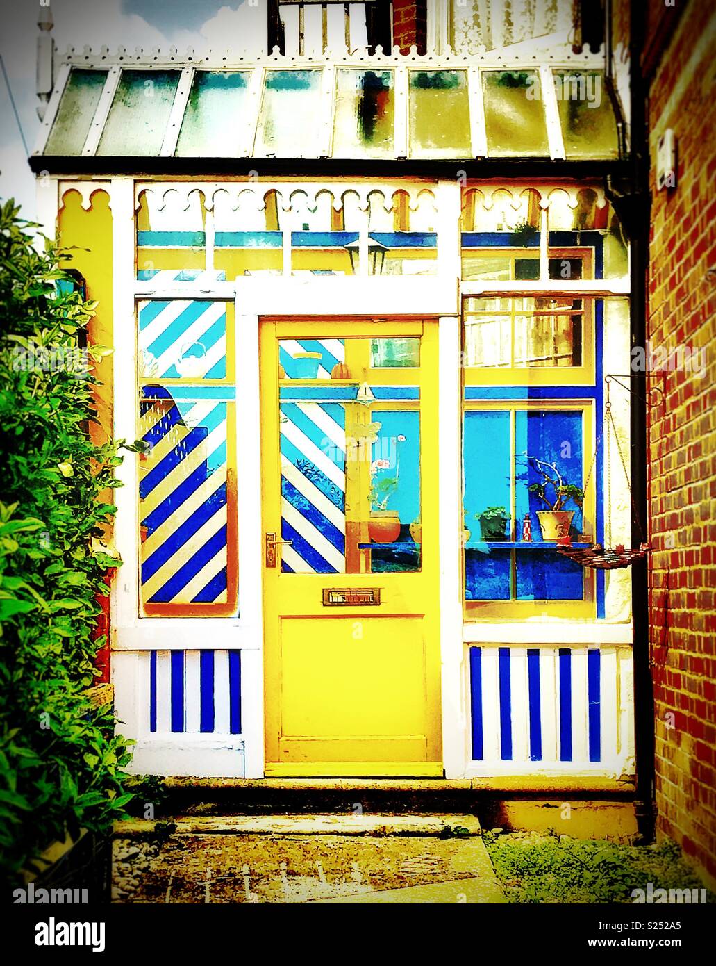Covered side entrance porch , Victorian style, with bright yellow door, blue and white striped panelling and glass sloping roof, Littlehampton , Sussex, UK Stock Photo