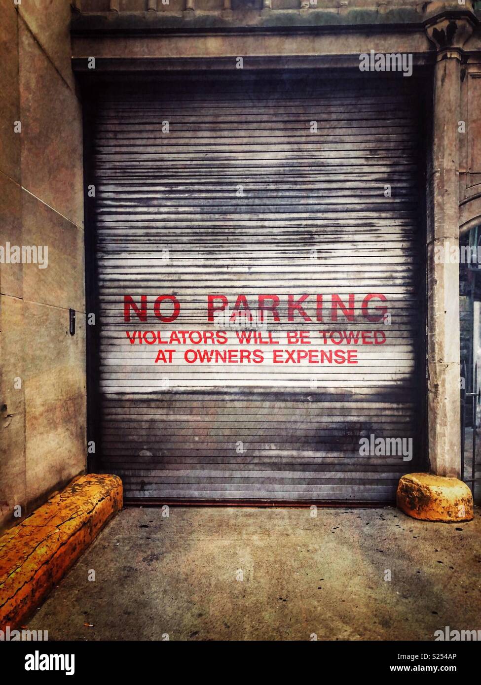 A metal garage door that says “No parking.  Violators will be towed at owners expense” Stock Photo