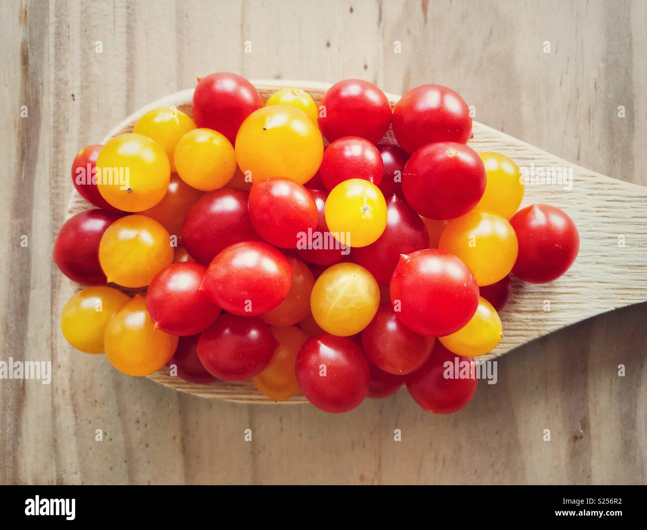 Closeup view of red and yellow Tomberry tomatoes in a wooden spoon on a wooden surface - Smartphone Captured Stock Image