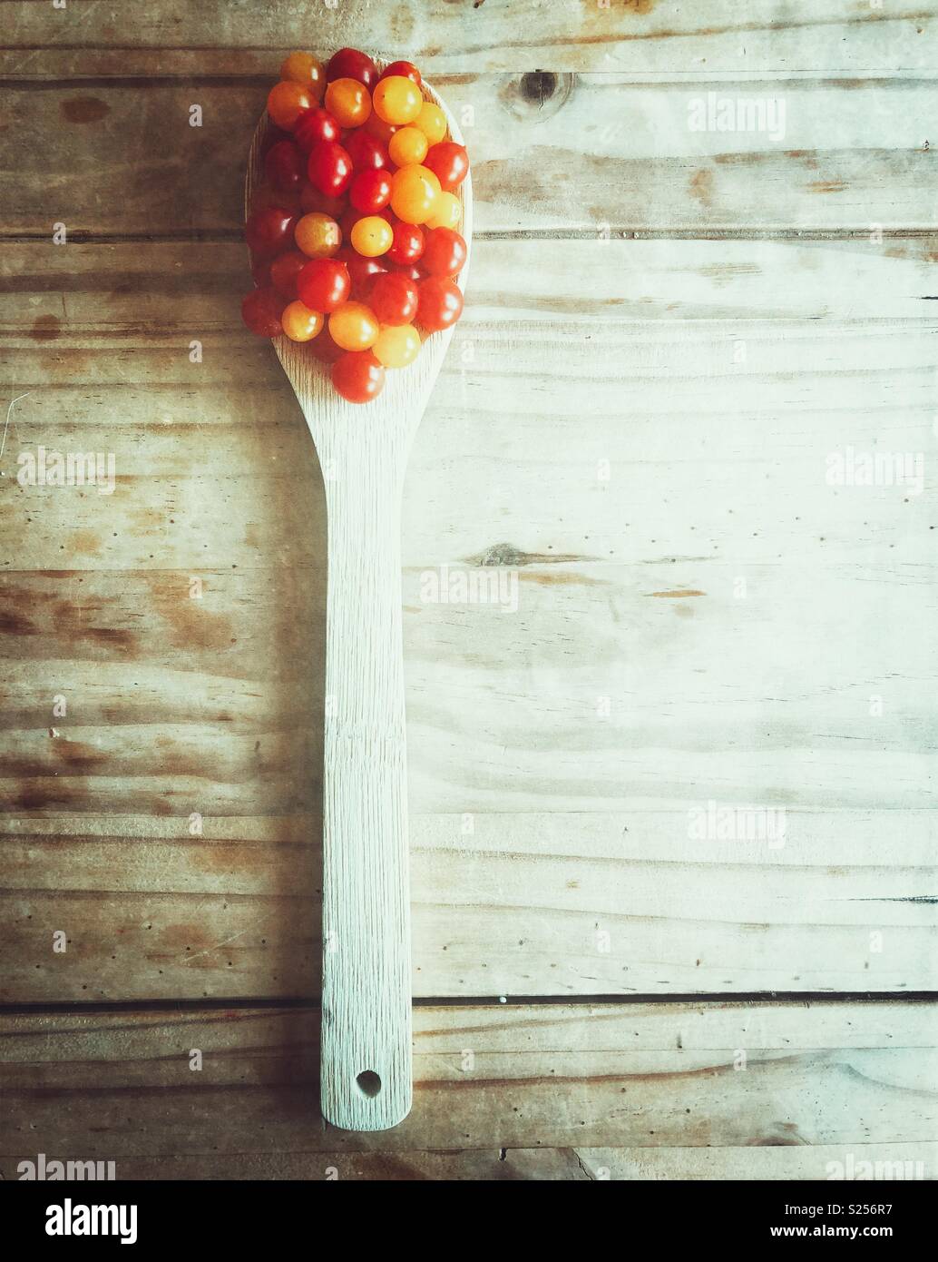 Spoonful of ripe red and yellow Tomberry tomatoes on a rustic wooden table - Smartphone Captured Stock Image