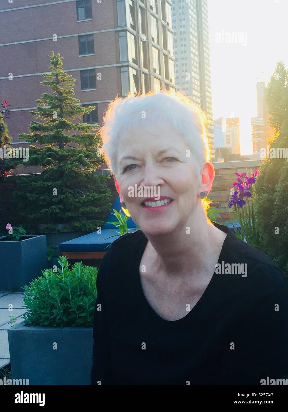 Mature woman with gray hair smiling on roof deck in midtown Manhattan, NYC, USA - Smartphone Captured Stock Image