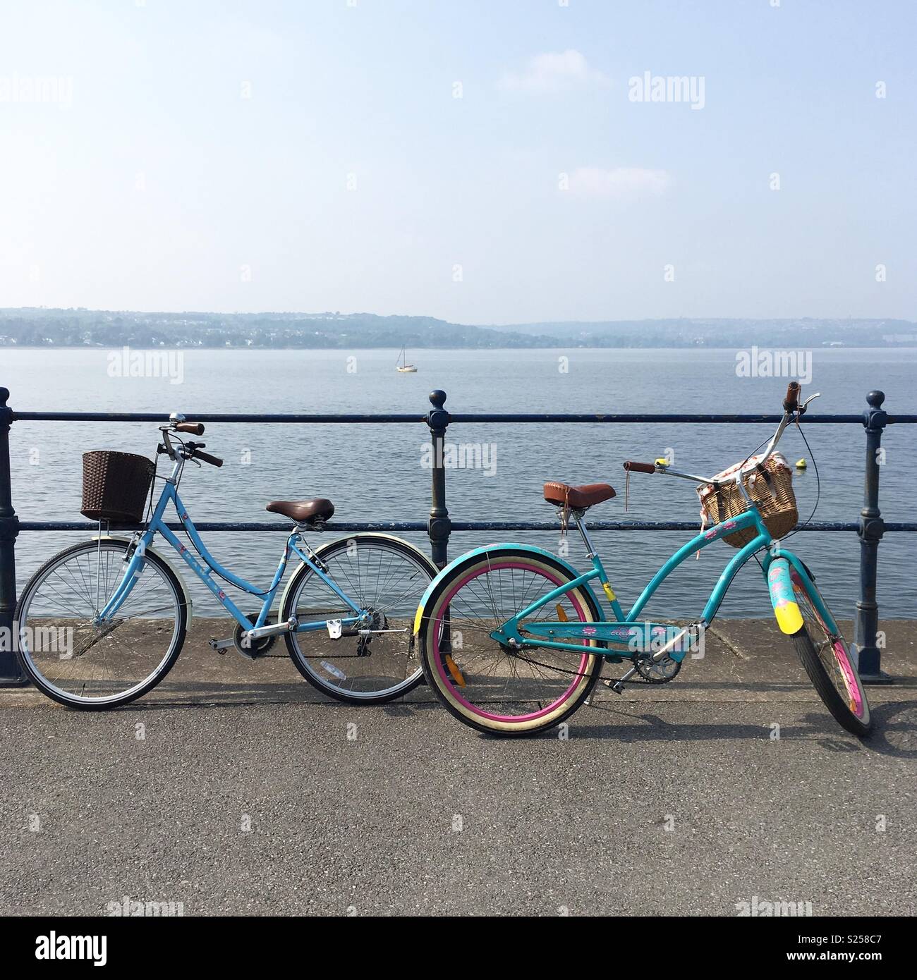 Two colourful bicycles against railings on the seafront at Mumbles, Swansea, South Wales - Smartphone Captured Stock Image