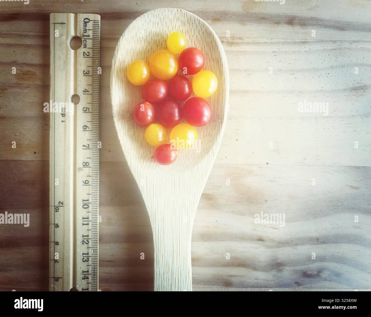 Red and yellow Tomberry tomatoes in a wooden spoon next to a wooden ruler - Smartphone Captured Stock Image