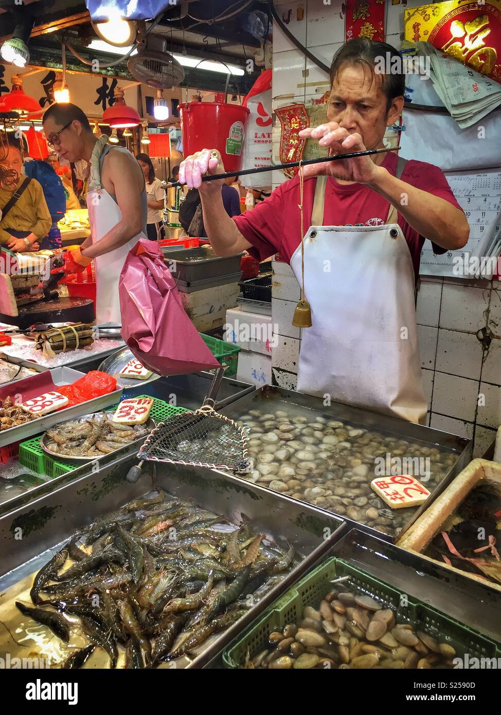 A fishmonger weighs produce using a traditional Chinese steelyard balance scale in a 'wet market', Yuen Long, New Territories, Hong Kong - Smartphone Captured Stock Image