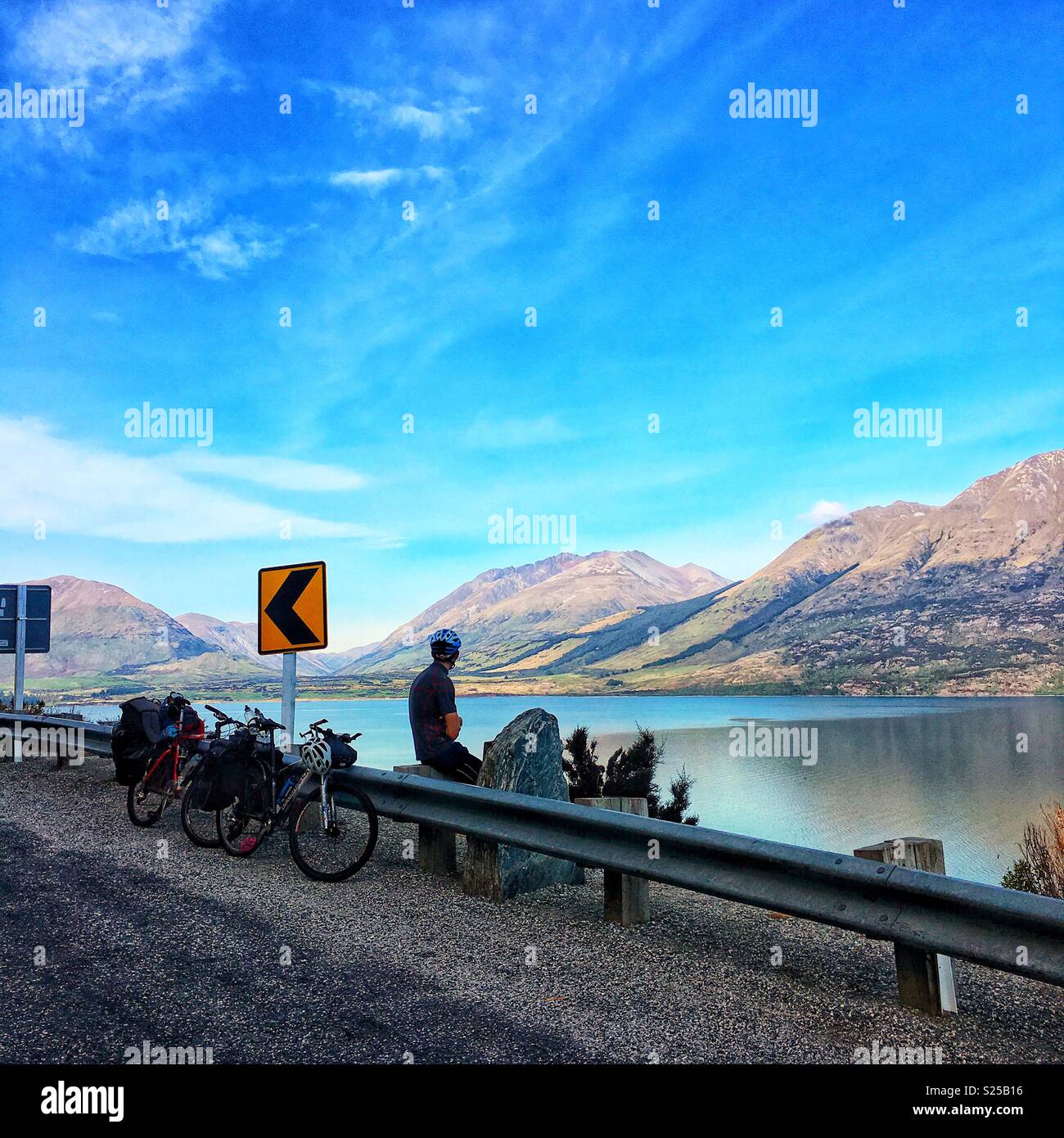 Cycle tourist taking in the crystal clear waters of Lake Wakatipu on a still morning, riding between Queenstown and Glenorchy. Stock Photo