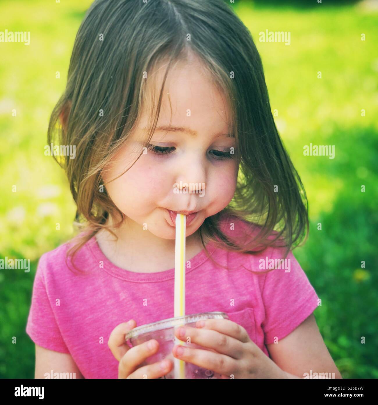 Toddler girl drinking juice from a plastic cup with a straw outside at