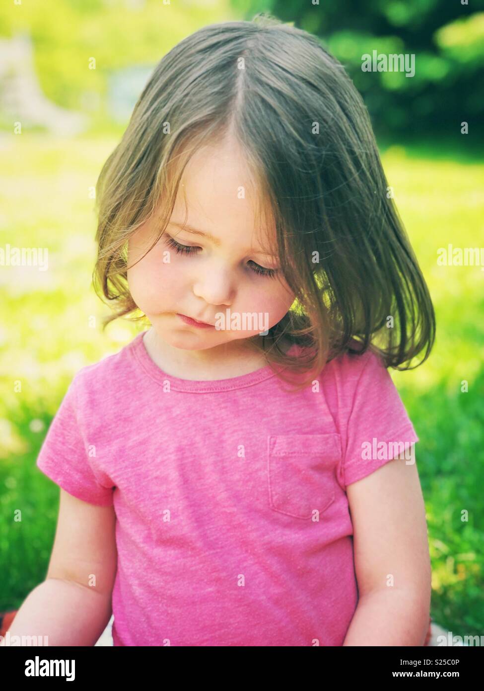 Candid portrait of 2 year old toddler child sitting outside on a sunny day Stock Photo