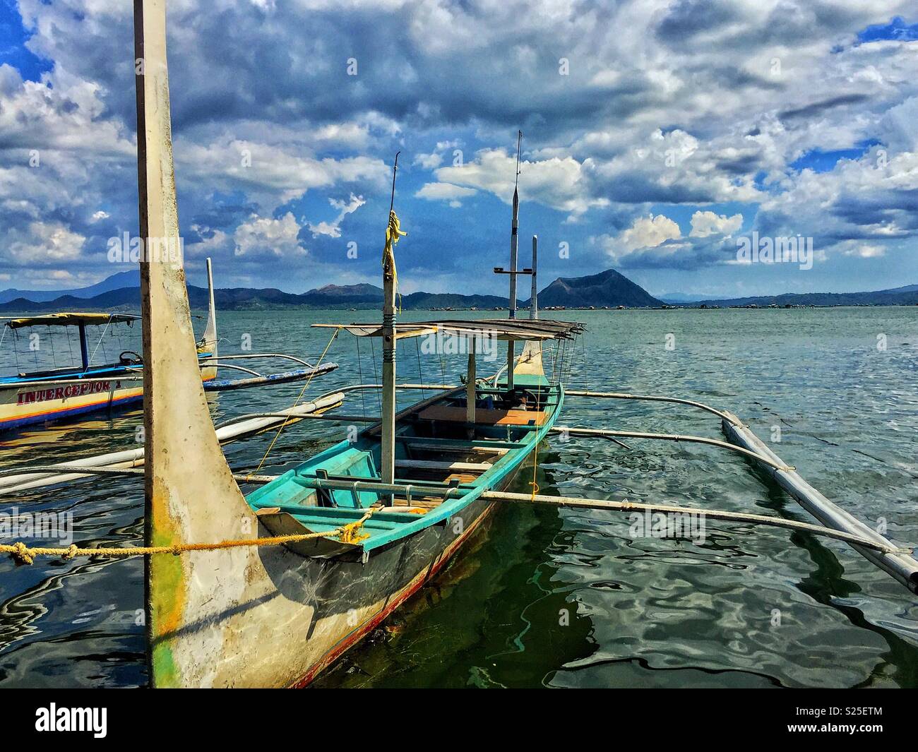 Traditional Filipino outrigger boats on the tranquil waters of Taal Lake, Philippines, with the iconic Taal Volcano rising in the distance - Smartphone Captured Stock Image