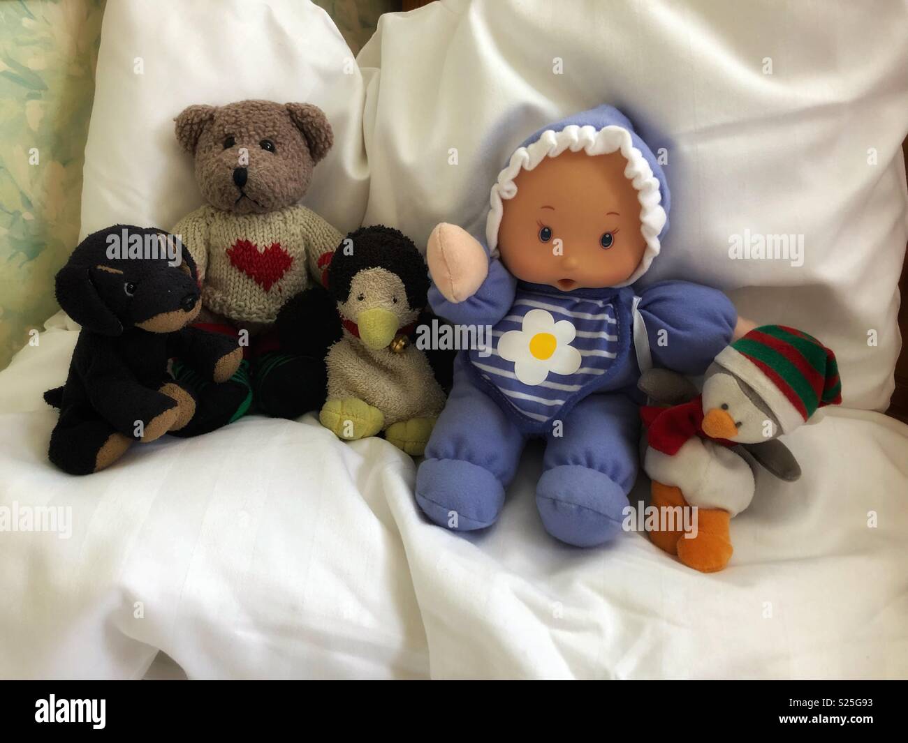 Stuffed animals and a baby doll sit comfortably on a big white pillow. - Smartphone Captured Stock Image