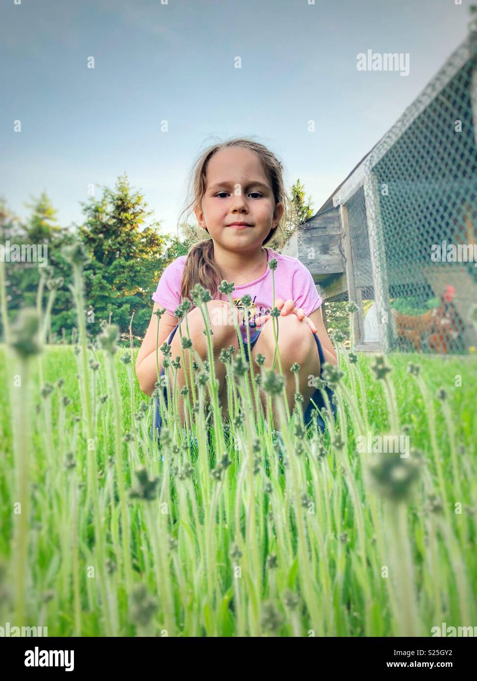 Young girl kneeling in backyard patch of weeds looking at camera Stock Photo