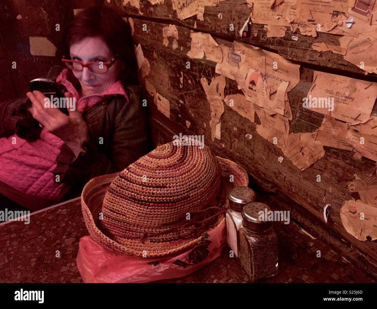 Woman with cellphone in a bar booth, with hat and salt and pepper shakers. - Smartphone Captured Stock Image