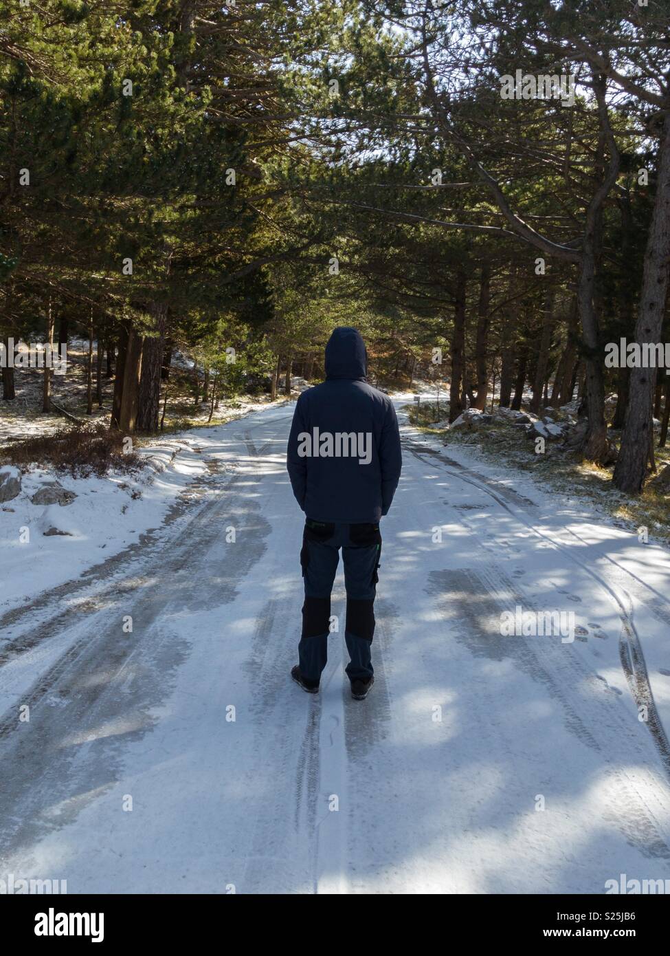 Man in warm jacket walking on frozen mountain road Stock Photo
