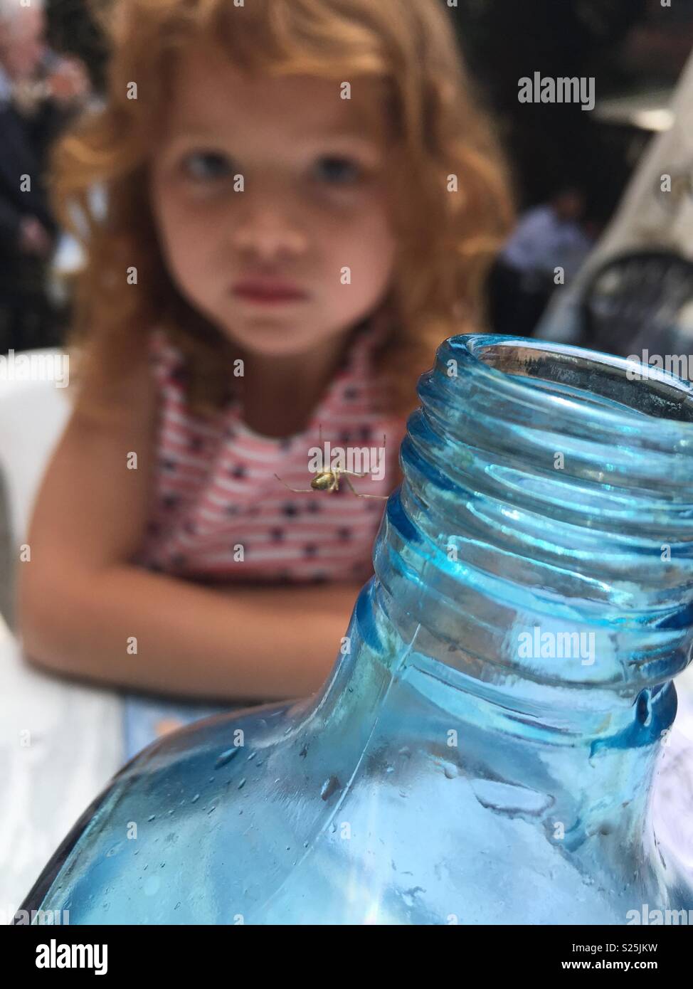 Little girl watching a spider spin a web on a water bottle in a restaurant Stock Photo