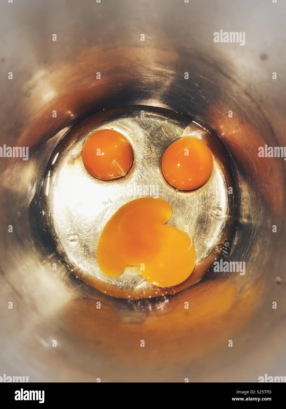 The yolk falls into a frying pan from a cracked raw egg, split by the