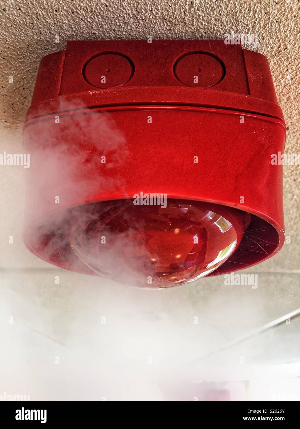 Close up image of a ceiling mounted fire alarm siren about to be engulfed by smoke. Where there's smoke there's fire - Smartphone Captured Stock Image