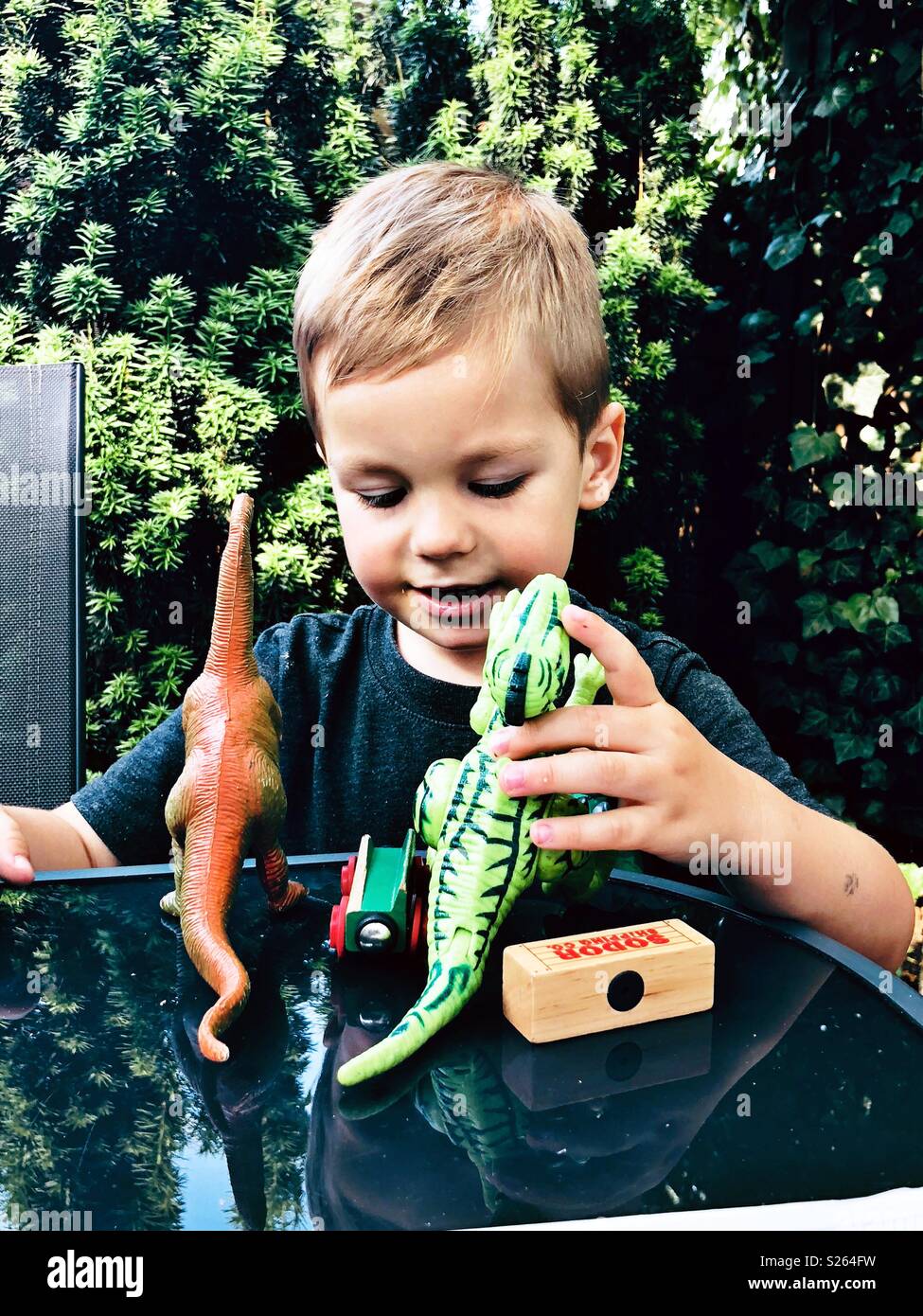 A boy playing with toy dinosaurs outside Stock Photo
