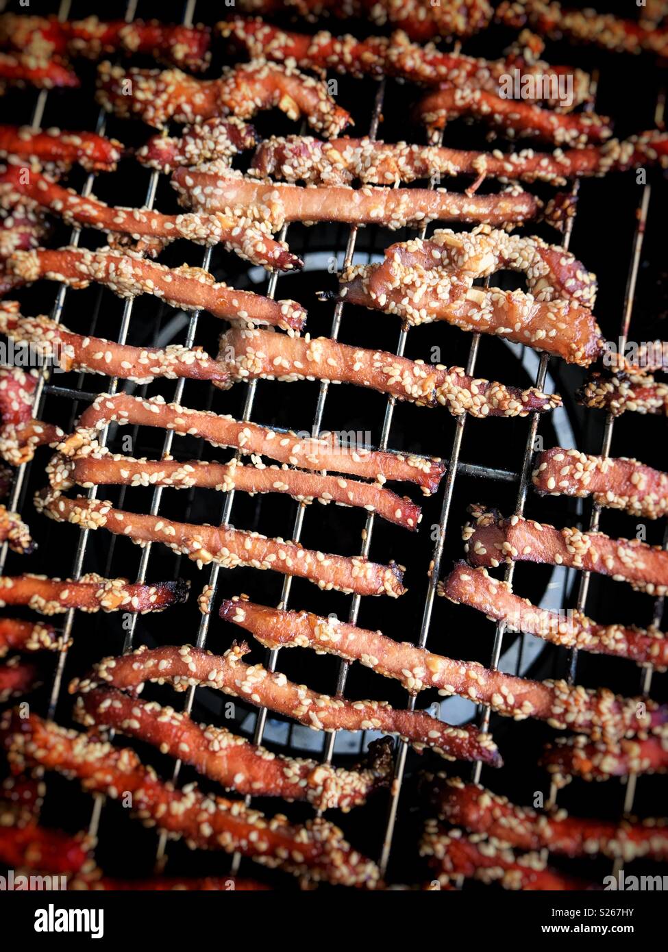 Pork strips coated with sesame seeds cooking on a barbecue - Smartphone Captured Stock Image