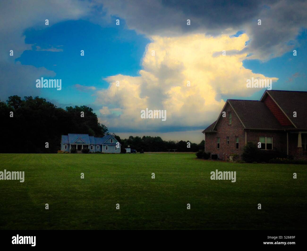 Green pastures, fluffy clouds, blue sky, two houses, and distant treeline in dreamy summer rural photo - Smartphone Captured Stock Image