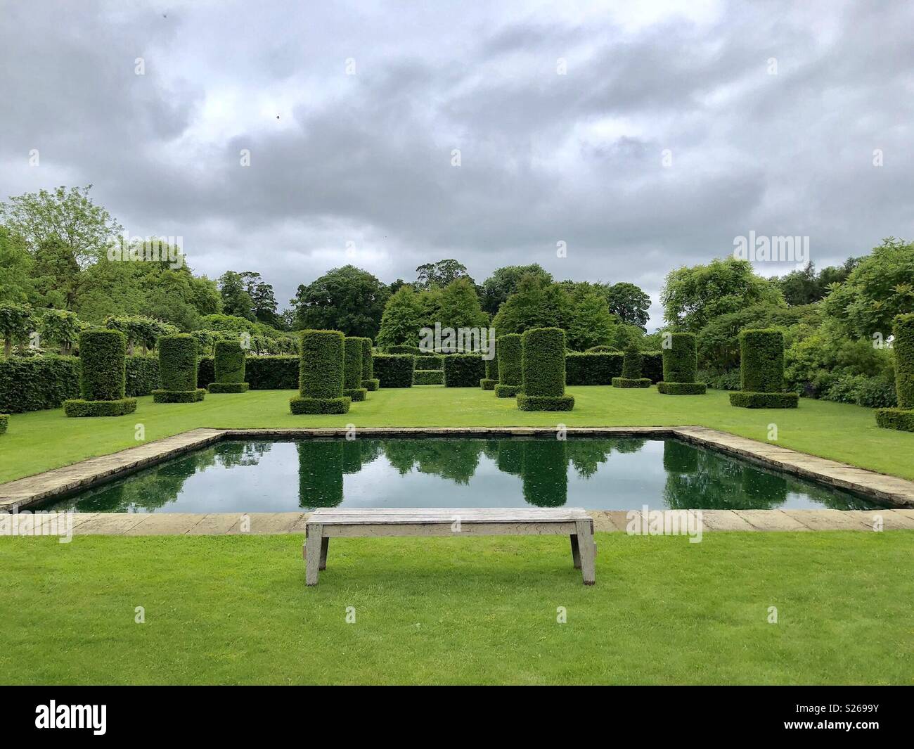 Oblong pond in topiary garden with a bench - Smartphone Captured Stock Image