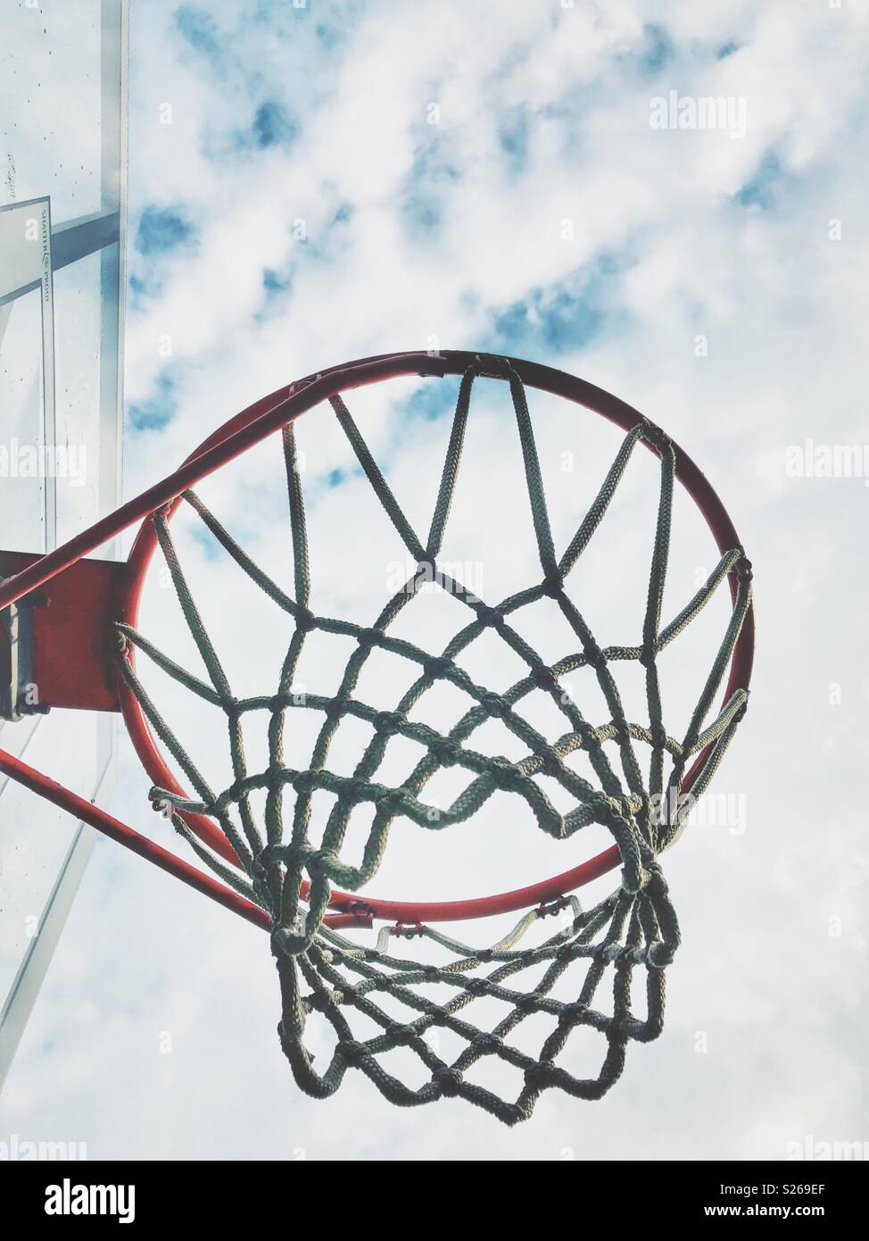 Looking up at a basketball hoop from the side with a cloudy blue sky in the background - Smartphone Captured Stock Image