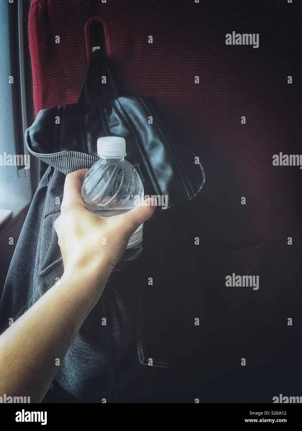 A hand reaches for a bottle of water from a black backpack - Smartphone Captured Stock Image