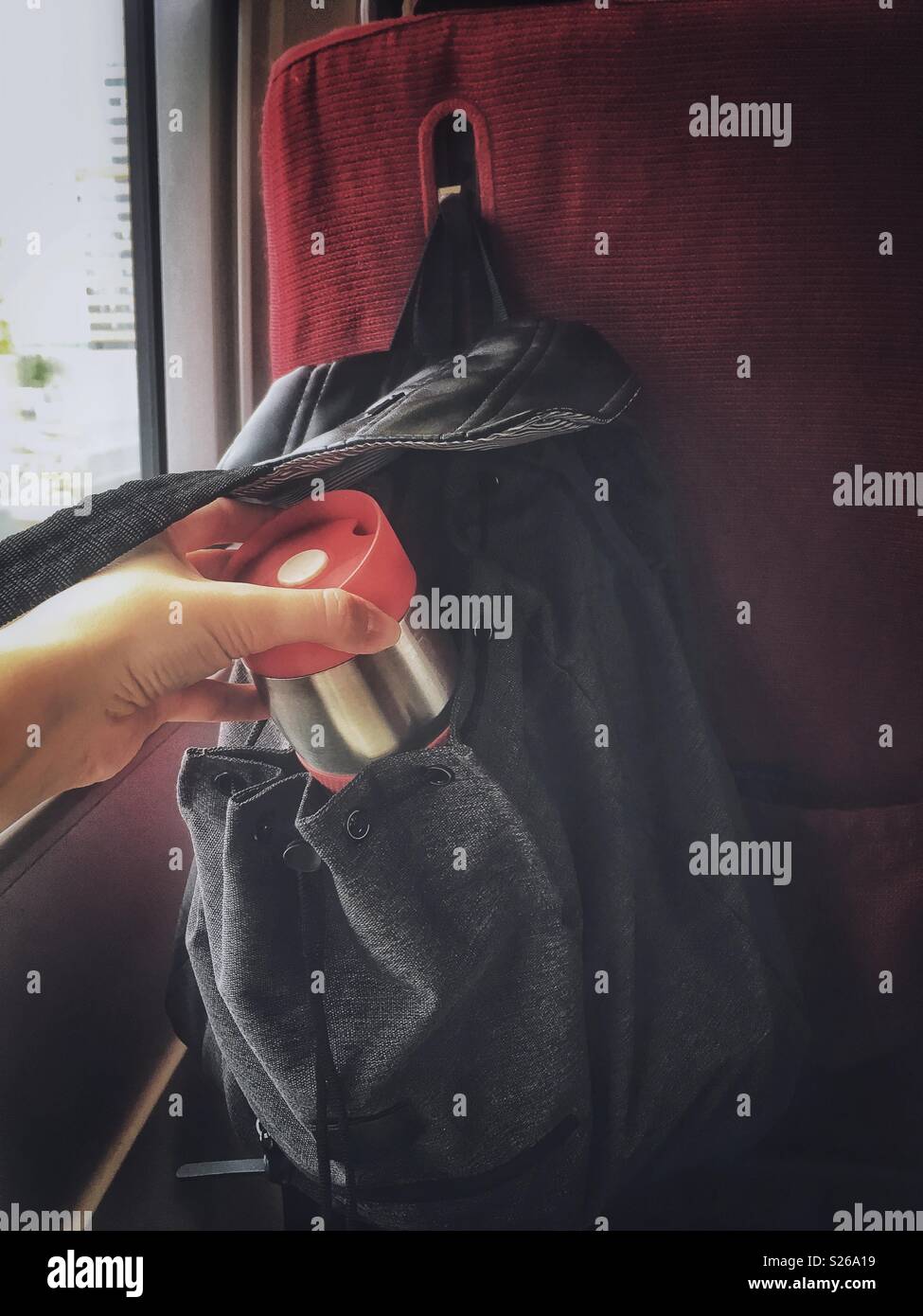 A hand reaches for a thermal cup from a backpack on a train - Smartphone Captured Stock Image