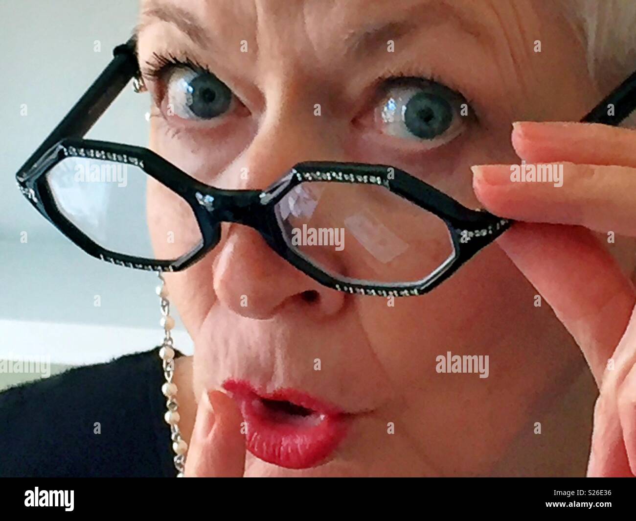 Librarian with vintage eyeglasses and neck chain signaling hush with her finger USA Stock Photo