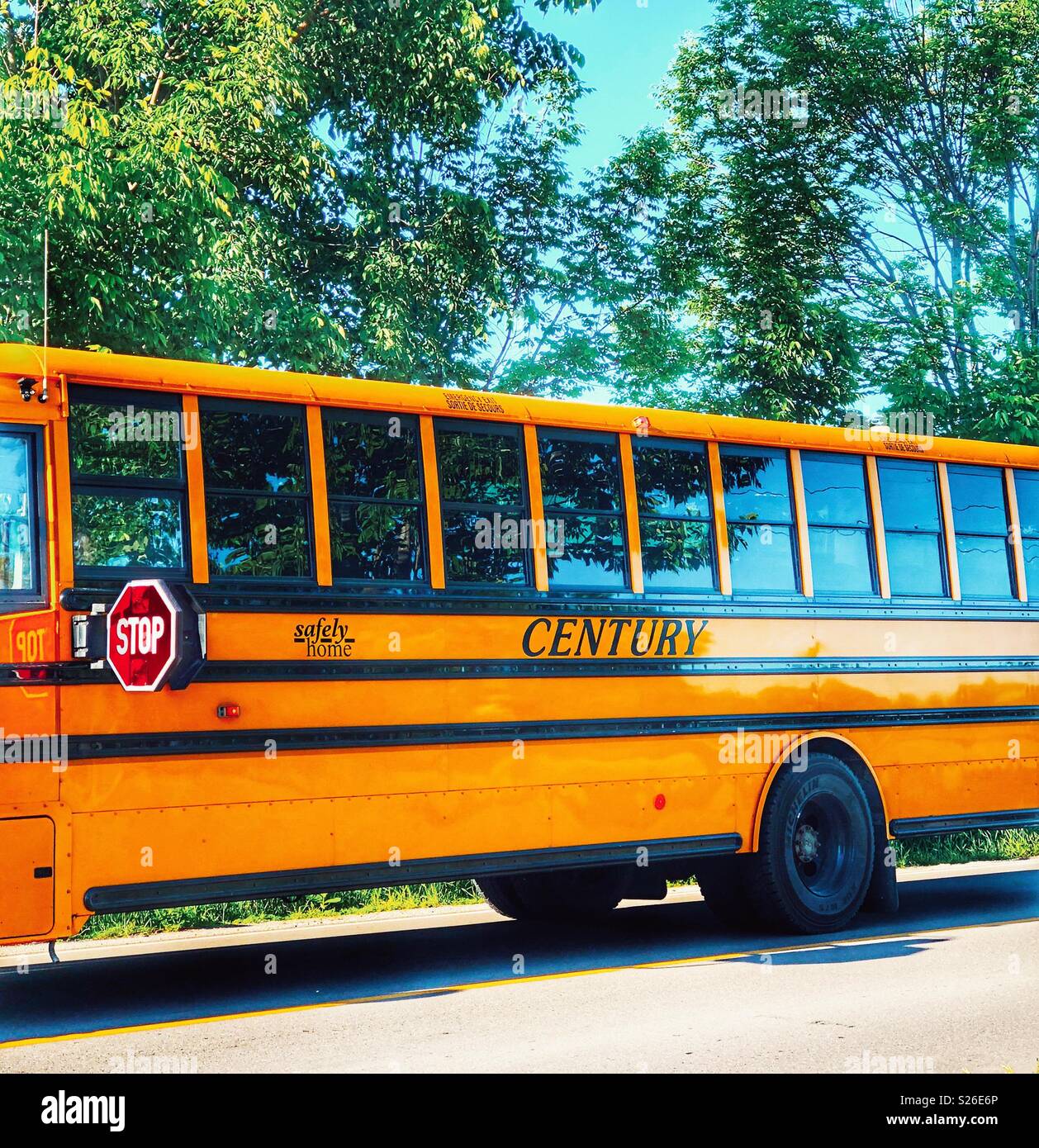 Century school bus with stop sign out on country road with blue sky and green trees reflecting in windows - Smartphone Captured Stock Image