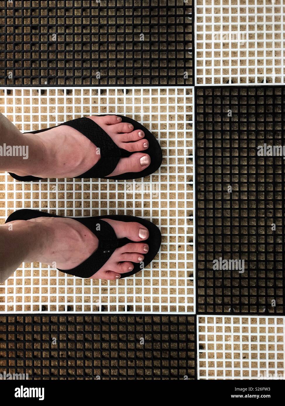 Feet in flip-flops on a black and white floor. - Smartphone Captured Stock Image