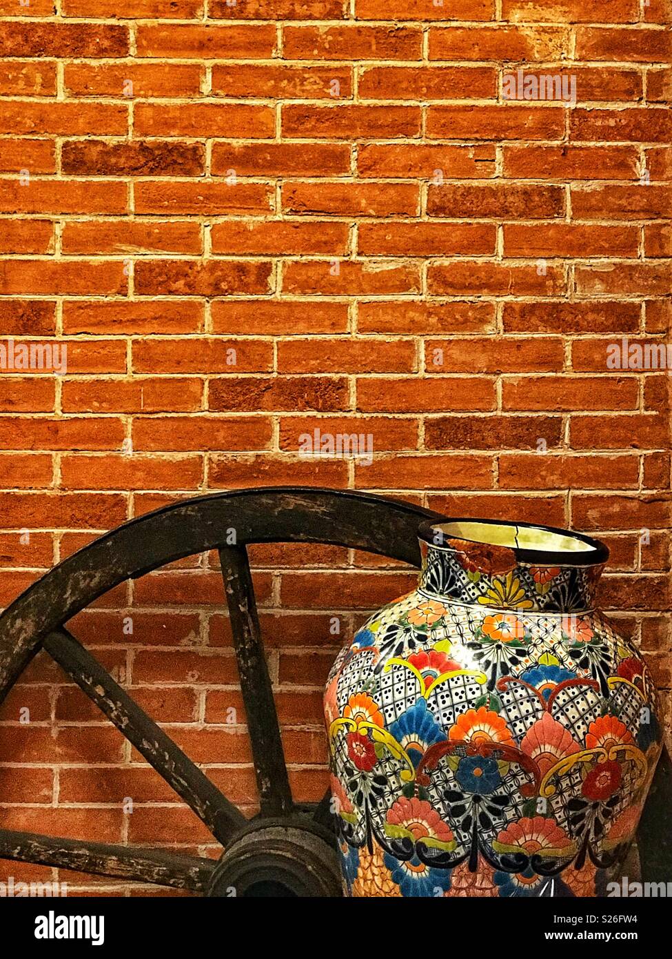 Old wheel and colourful vase against a brick wall. - Smartphone Captured Stock Image